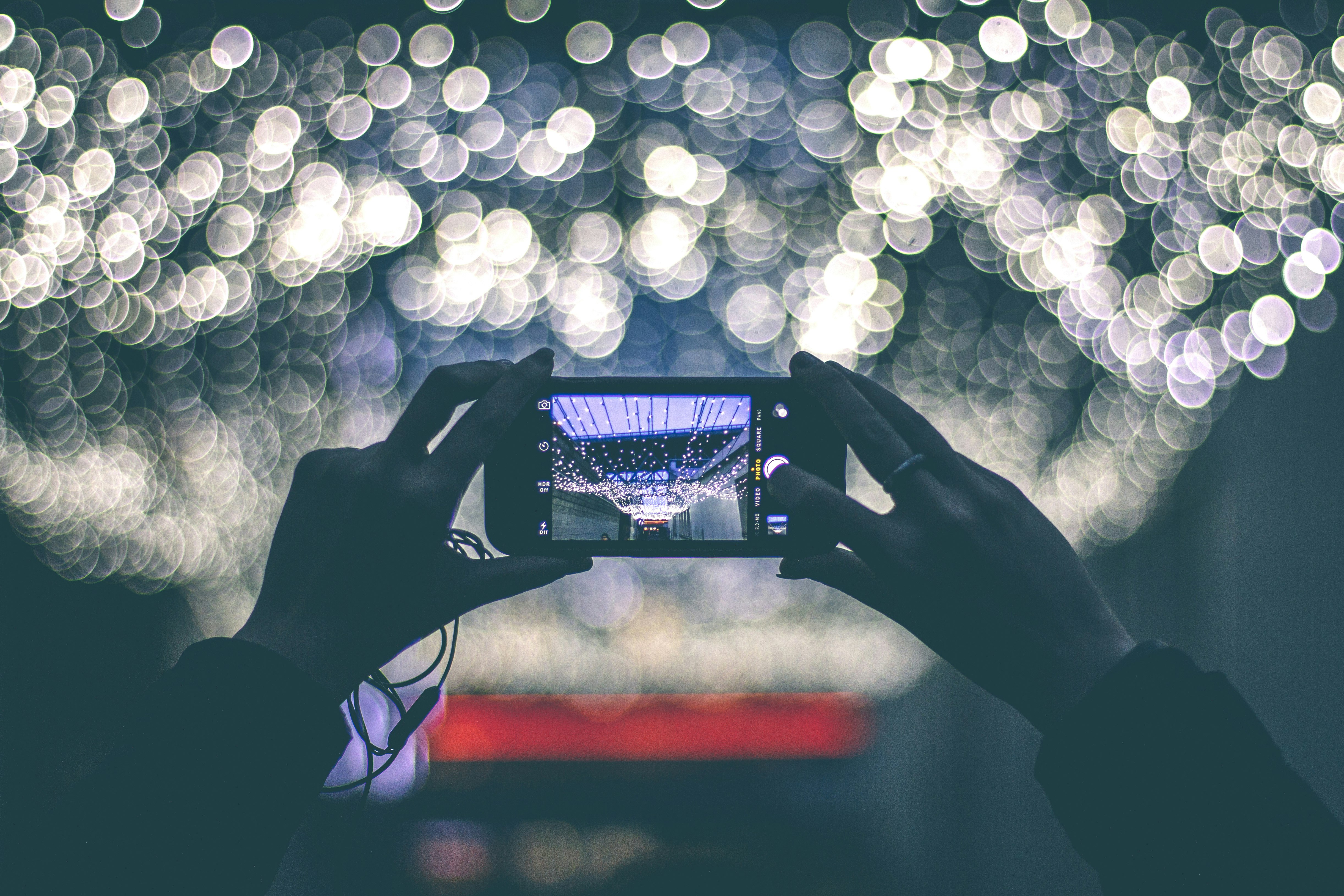 selective focus photography of person holding smartphone while taking picture of scenery